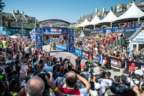 Cyclists race through a crowded finish line with enthusiastic spectators.