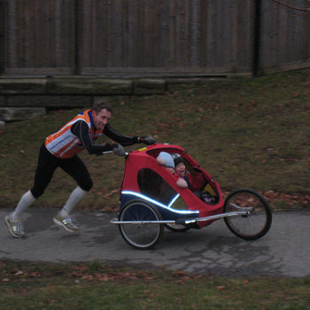 Person pushing a child in a jogging stroller outdoors.