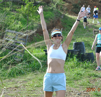 Woman celebrating outdoors in athletic wear with arms raised.