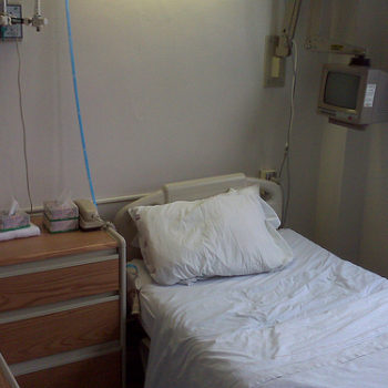 A simple hospital room with a single bed and bedside table.