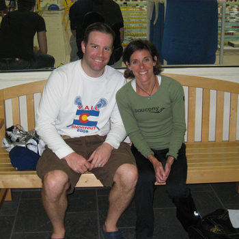 Two people sitting on a bench, smiling at the camera.