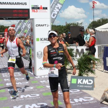 Athlete celebrating victory at a triathlon finish line holding a bouquet.