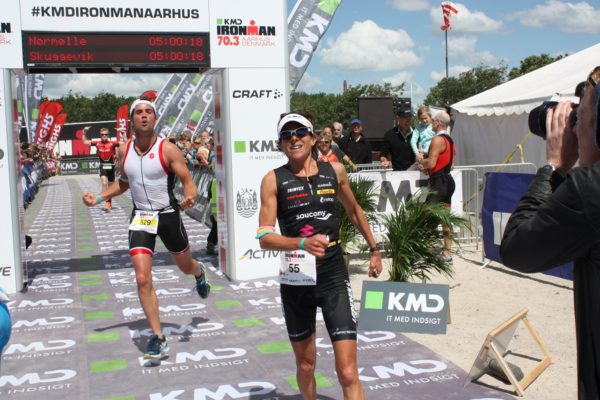 Athlete celebrating victory at a triathlon finish line holding a bouquet.