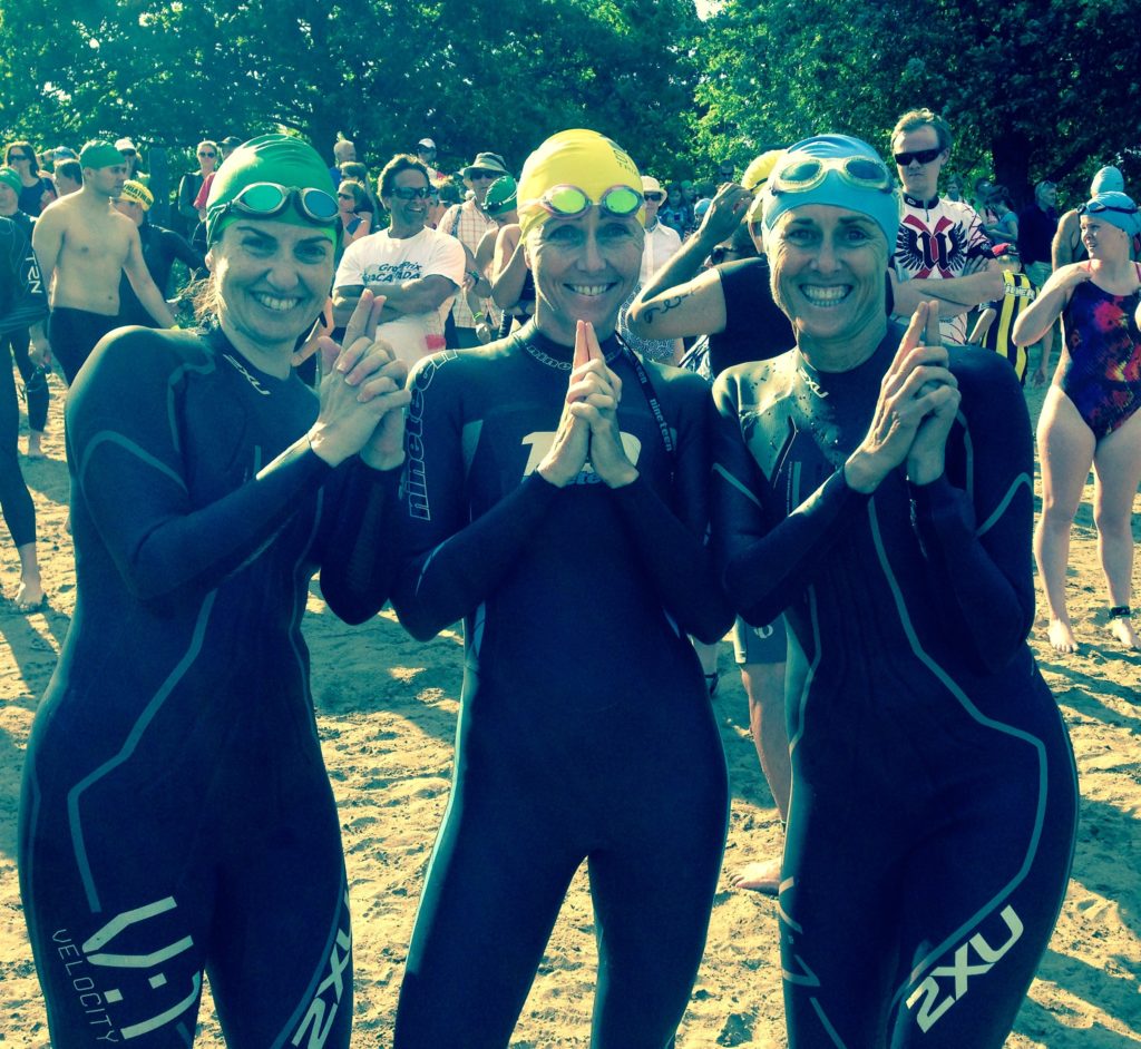 Three swimmers in wetsuits giving thumbs up at a swim event.