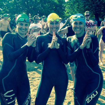 Three swimmers in wetsuits giving thumbs up at a swim event.