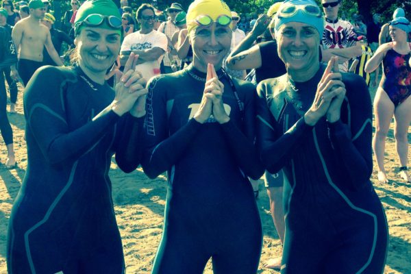 Three swimmers in wetsuits giving thumbs up at a swim event.