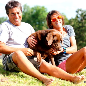 Happy couple sitting on grass with their dog on a sunny day.