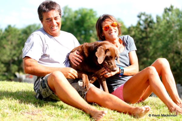 Happy couple sitting on grass with their dog on a sunny day.