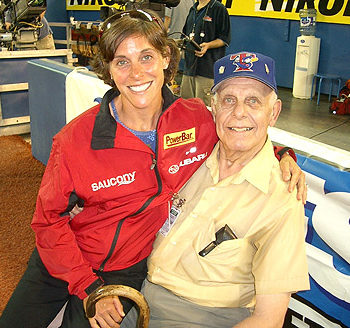 Smiling woman in red jacket with elderly man in cap at a gym.