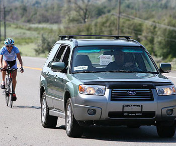 A green SUV driving on a road with a cyclist nearby.