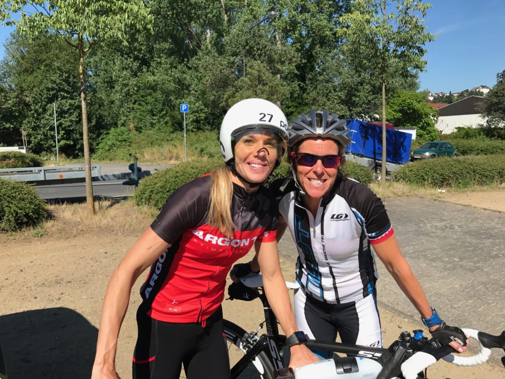 Two cyclists smiling and posing outdoors with their bikes.