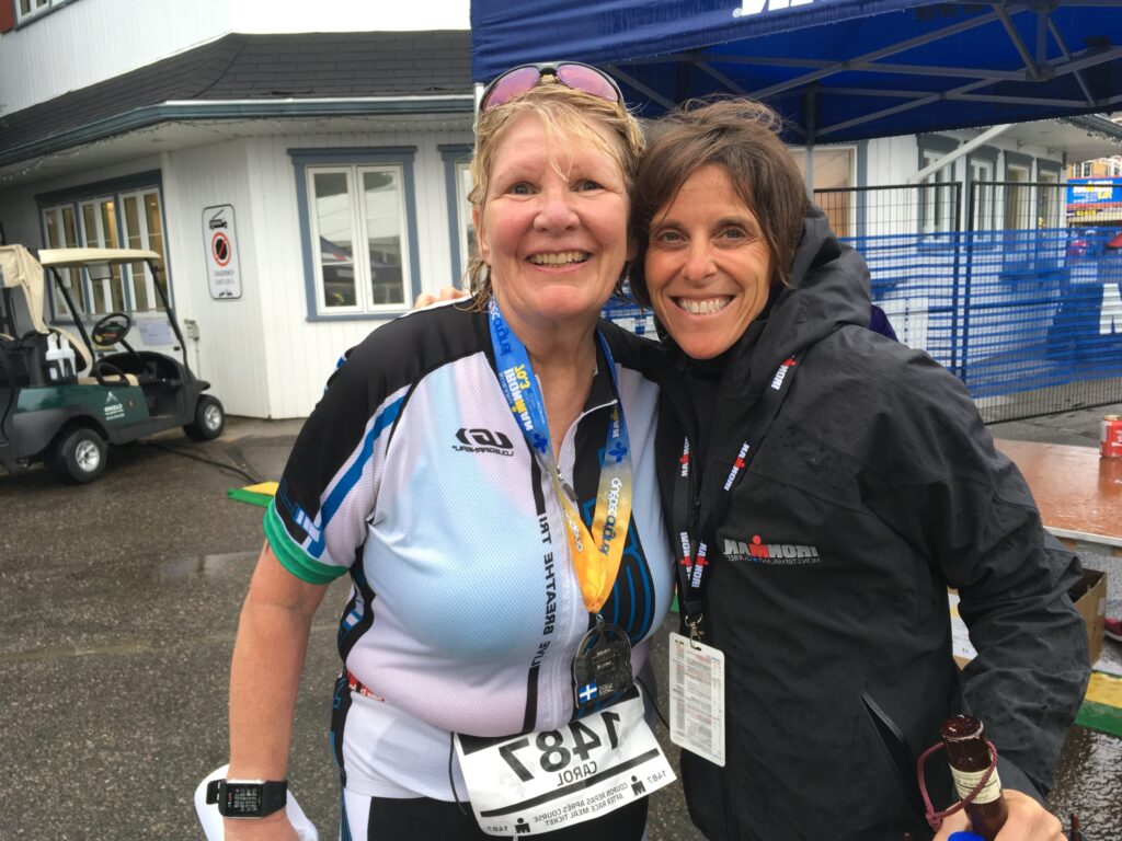 Two smiling women posing together outdoors, one with a race bib.