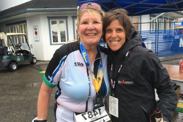 Two smiling women posing together outdoors, one with a race bib.