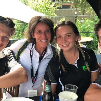 Four people smiling around a table outdoors with drinks.