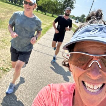 Three people jogging outdoors on a sunny day, smiling and enjoying the exercise.