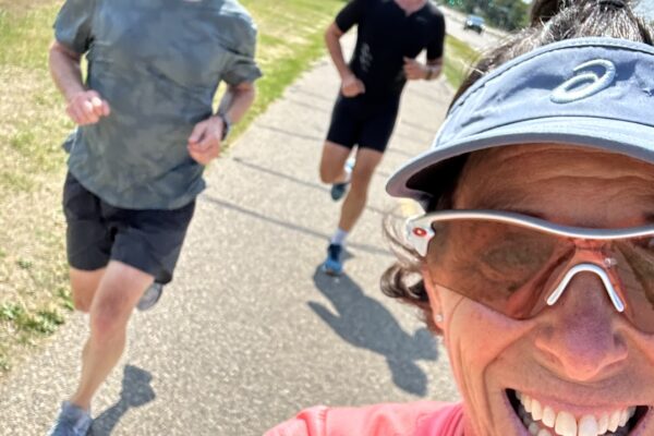 Three people jogging outdoors on a sunny day, smiling and enjoying the exercise.