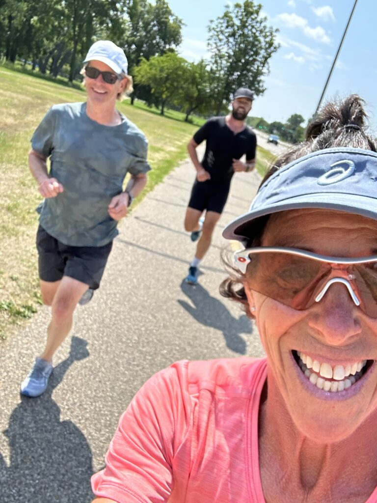 Three people jogging outdoors on a sunny day, smiling and enjoying the exercise.