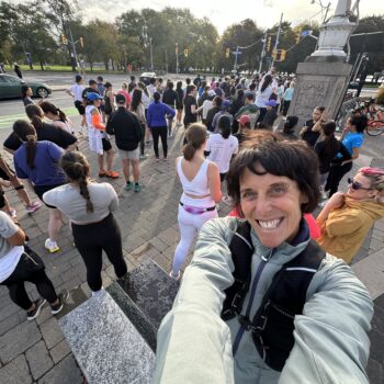 A cheerful person takes a selfie at a crowded outdoor event near a park.