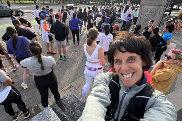 A cheerful person takes a selfie at a crowded outdoor event near a park.