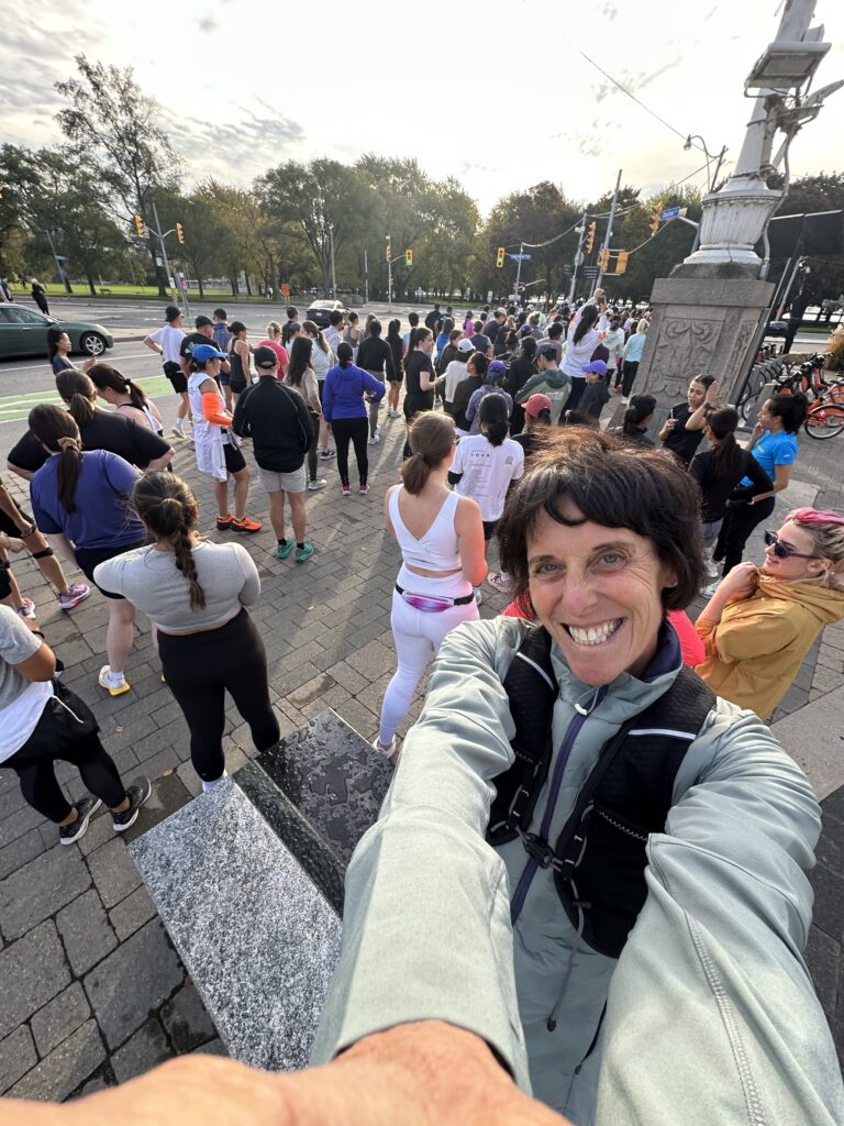 A cheerful person takes a selfie at a crowded outdoor event near a park.