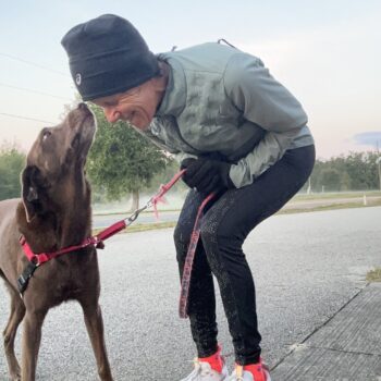Person bending down to kiss a dog on a leash outdoors.