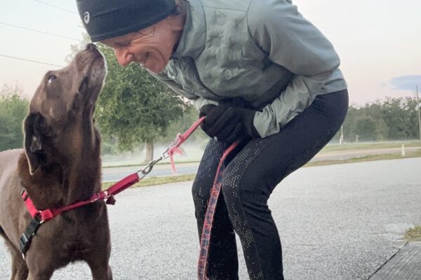 Person bending down to kiss a dog on a leash outdoors.