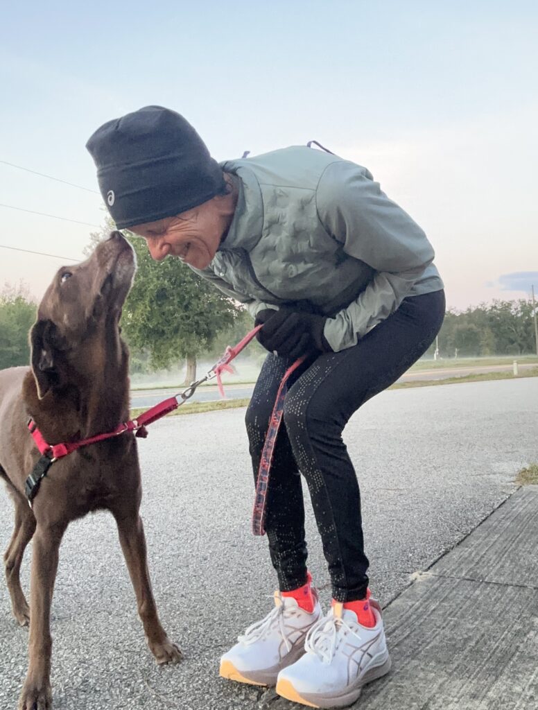 Person bending down to kiss a dog on a leash outdoors.